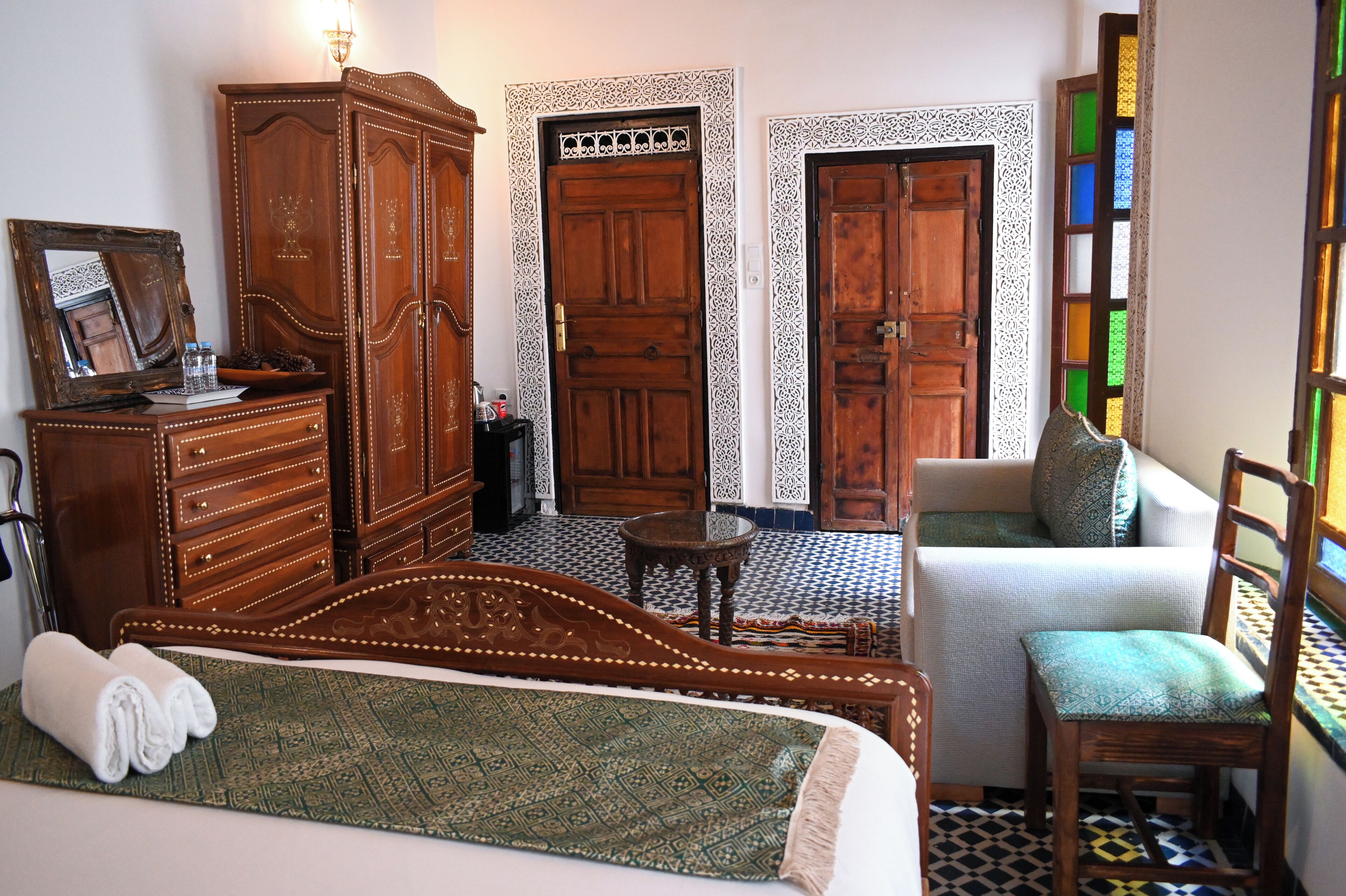 A room with a bed, a wooden wardrobe, a small table, a sofa, and a chair.