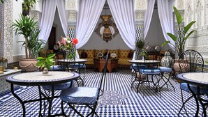 Une pièce avec des carreaux de sol à motifs, un canapé, deux tables avec des chaises et un élément décoratif mural.