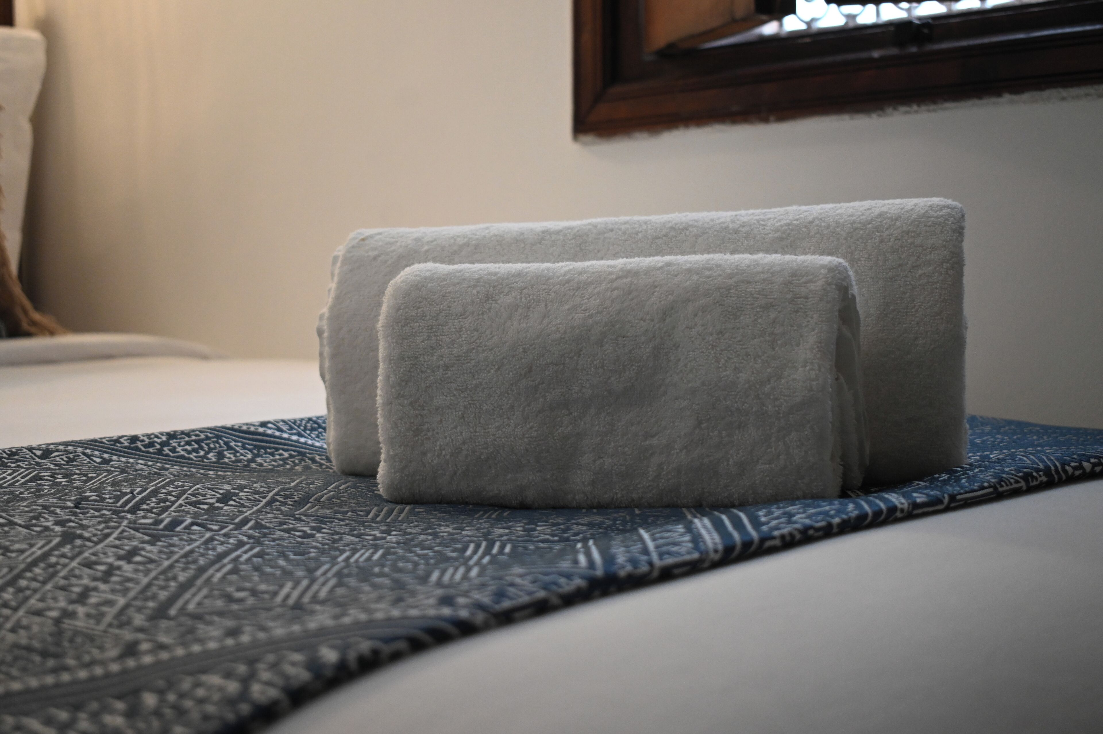 Ein ordentlich bezogenes Bett mit einer gemusterten Tagesdecke und zwei gefalteten Handtüchern.