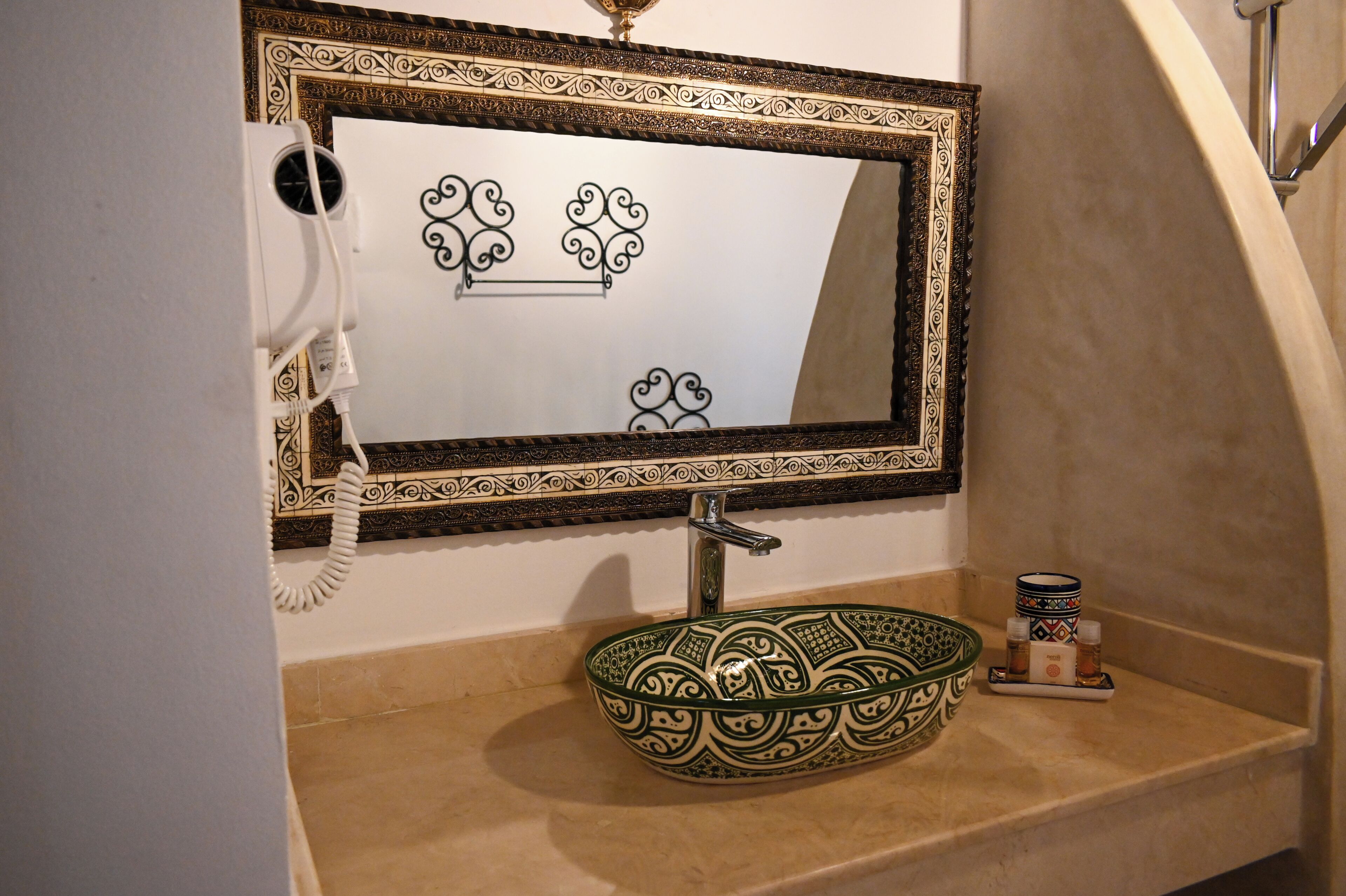 A bathroom with a decorative mirror, a green bowl sink, and a small shelf with toiletries.