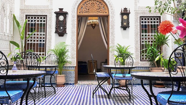 Une cour ornée de carreaux décoratifs, une arche centrale et des tables avec des chaises.