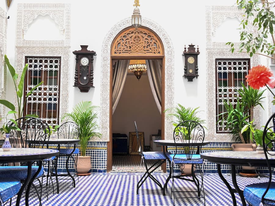 Un patio con baldosas estampadas, un arco central y mesas con sillas.