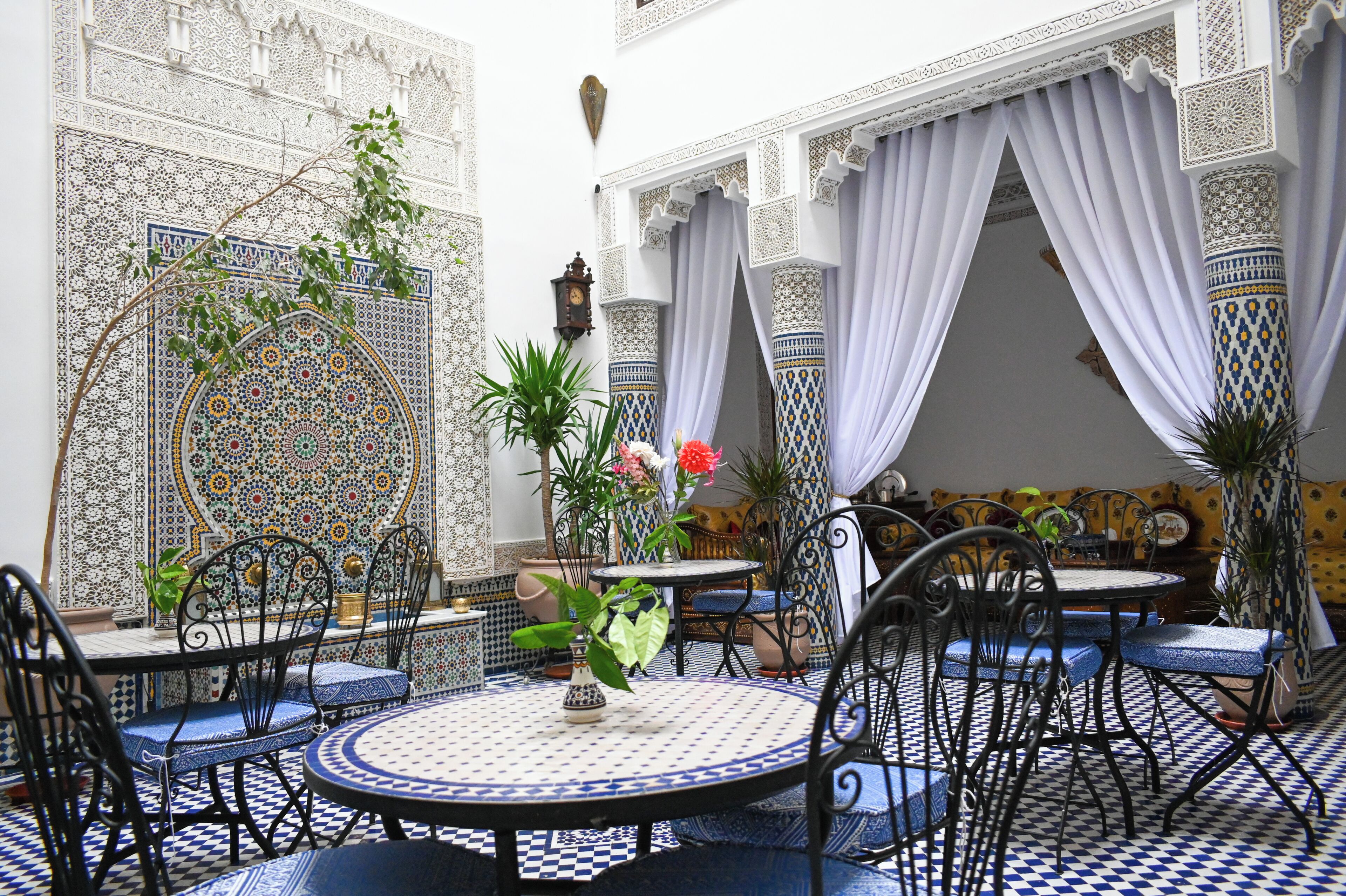 Un interior marroquí con paredes de azulejos estampados, una mesa redonda con sillas y un arco decorativo.