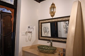Een badkamer met een grote spiegel, een haardroger, een wastafel met decoratieve kom en een telefoon op de muur.
