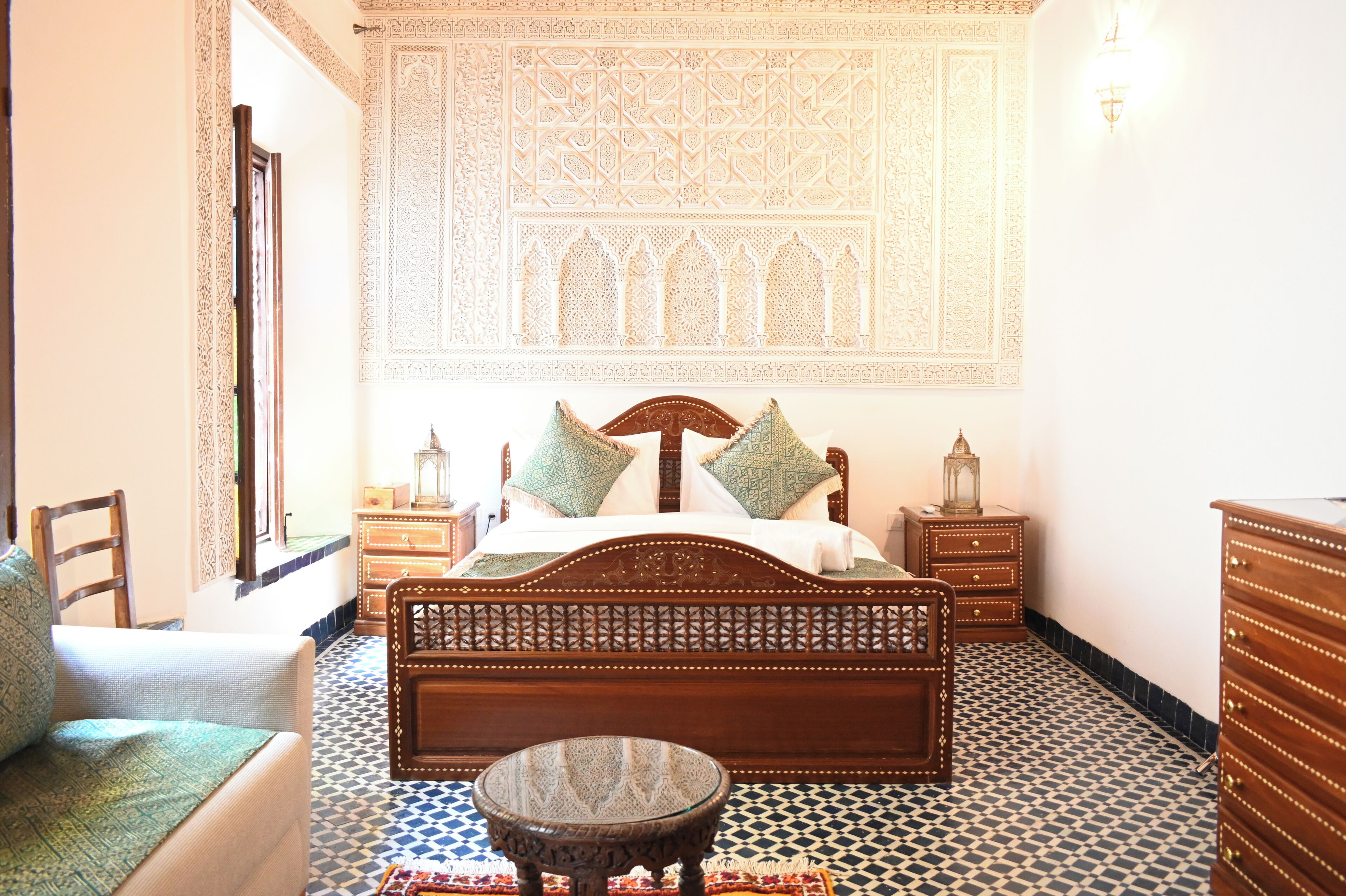 Una habitación con una cama, una silla, una mesita y un aparador.