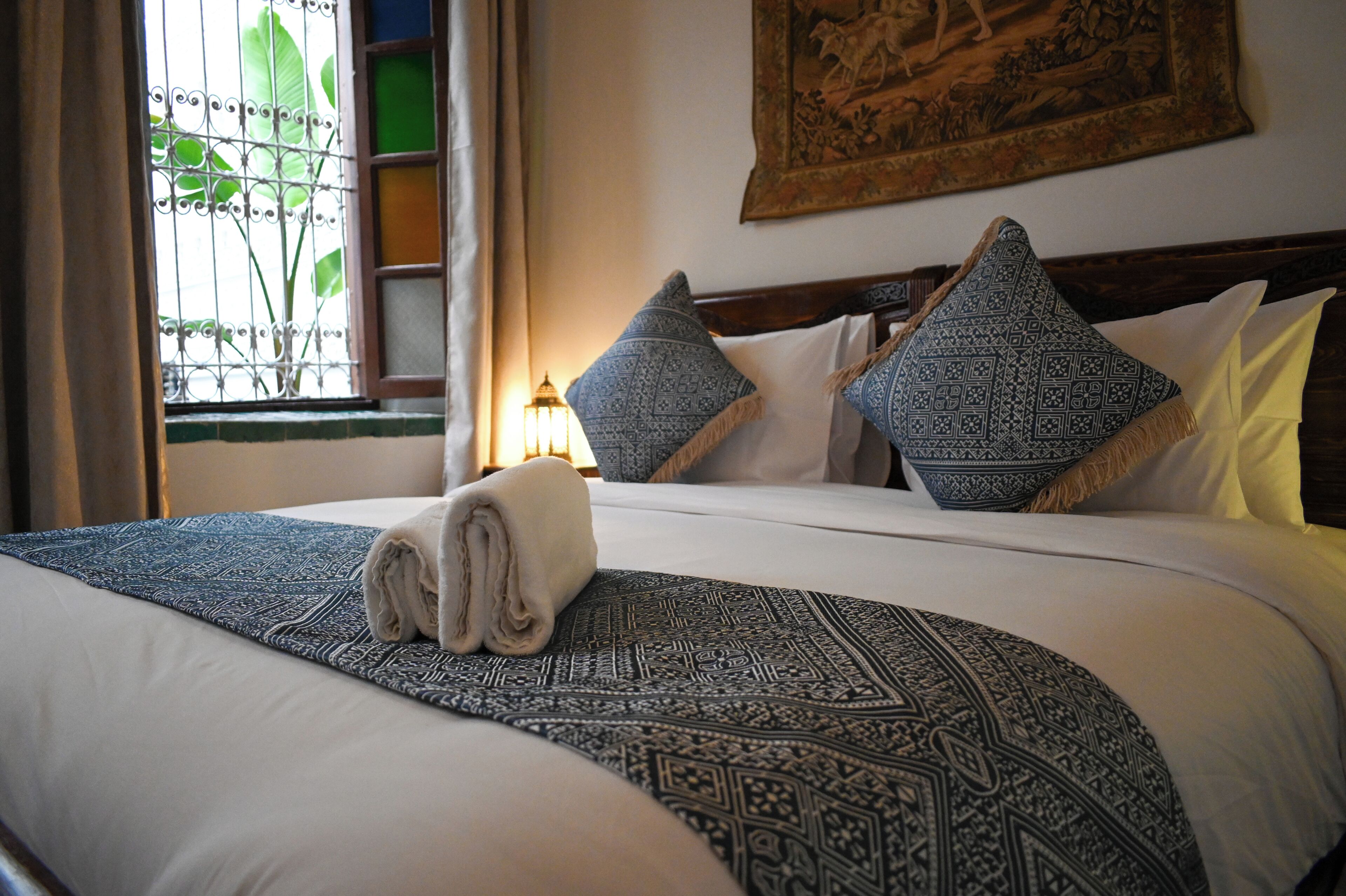 Una cama bien hecha con cubrecamas estampados, almohadas y una toalla enrollada.
