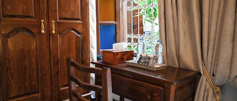 Un bureau en bois avec une chaise, une fenêtre avec des barreaux en métal et un rideau.