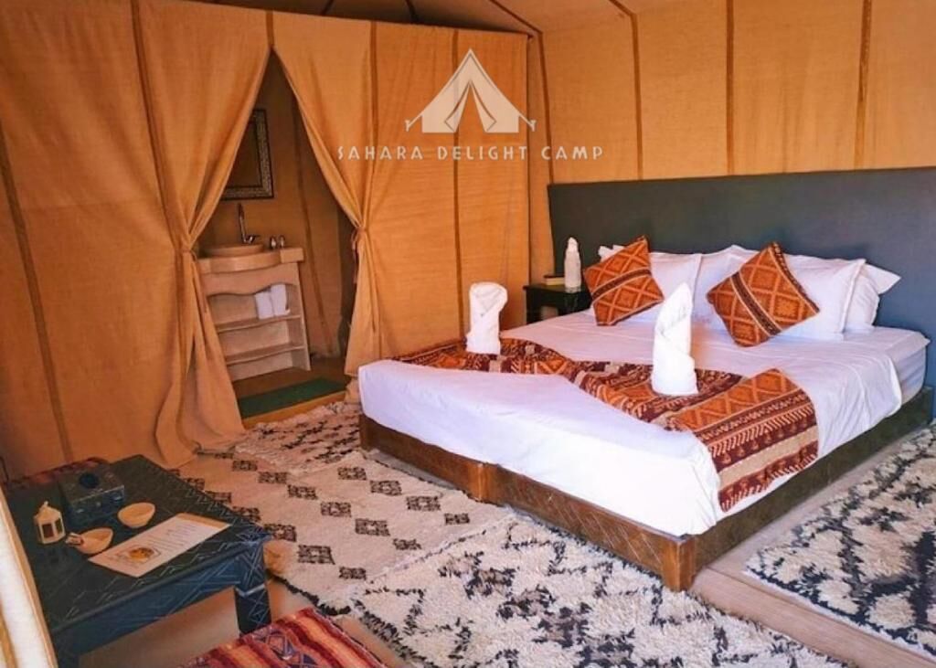 A bedroom with a bed, pillows, a nightstand, a small table with a teapot, and a wall-mounted shelf.