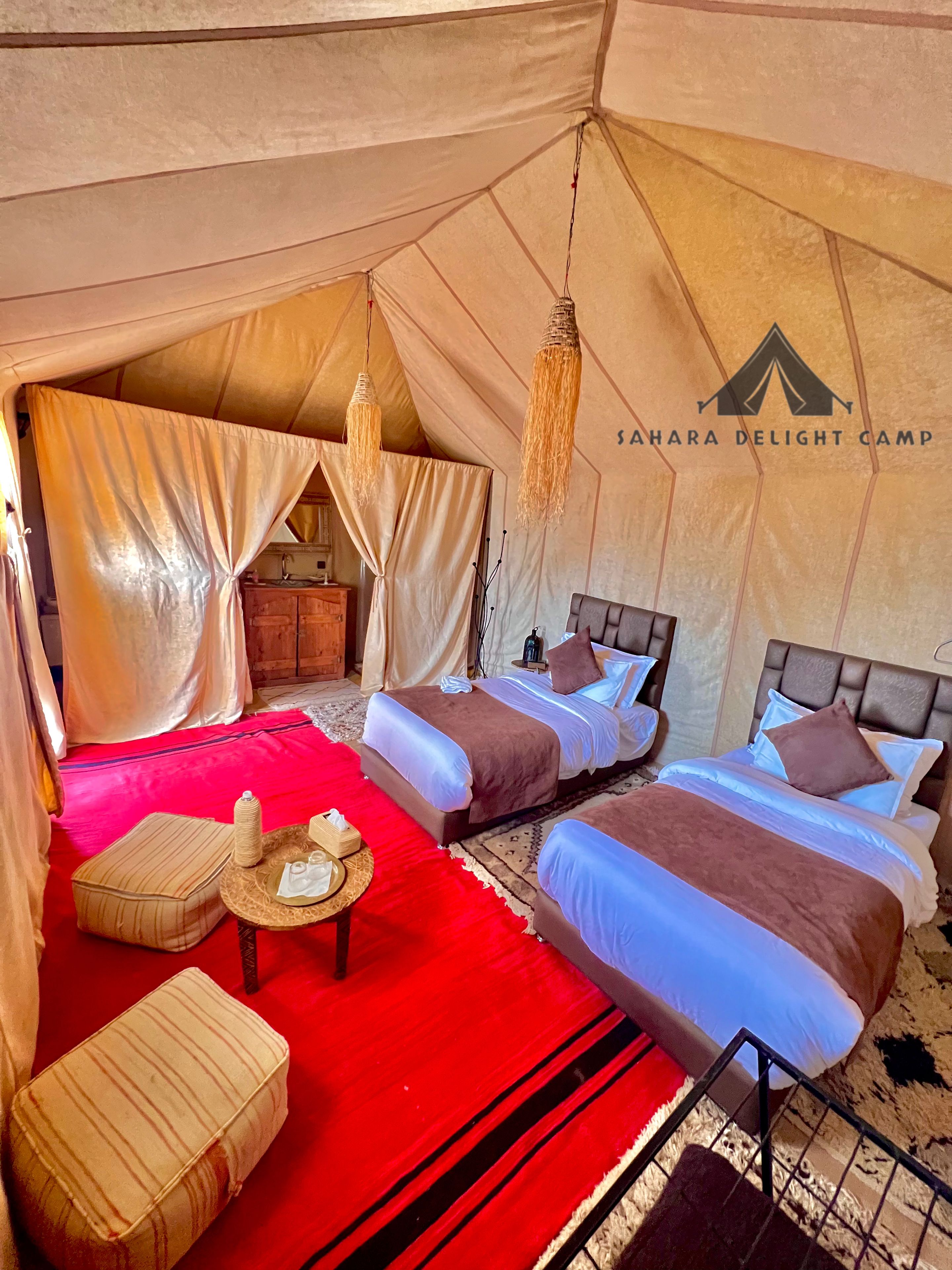 A tented accommodation with two beds, a red carpet, and a small table with amenities.