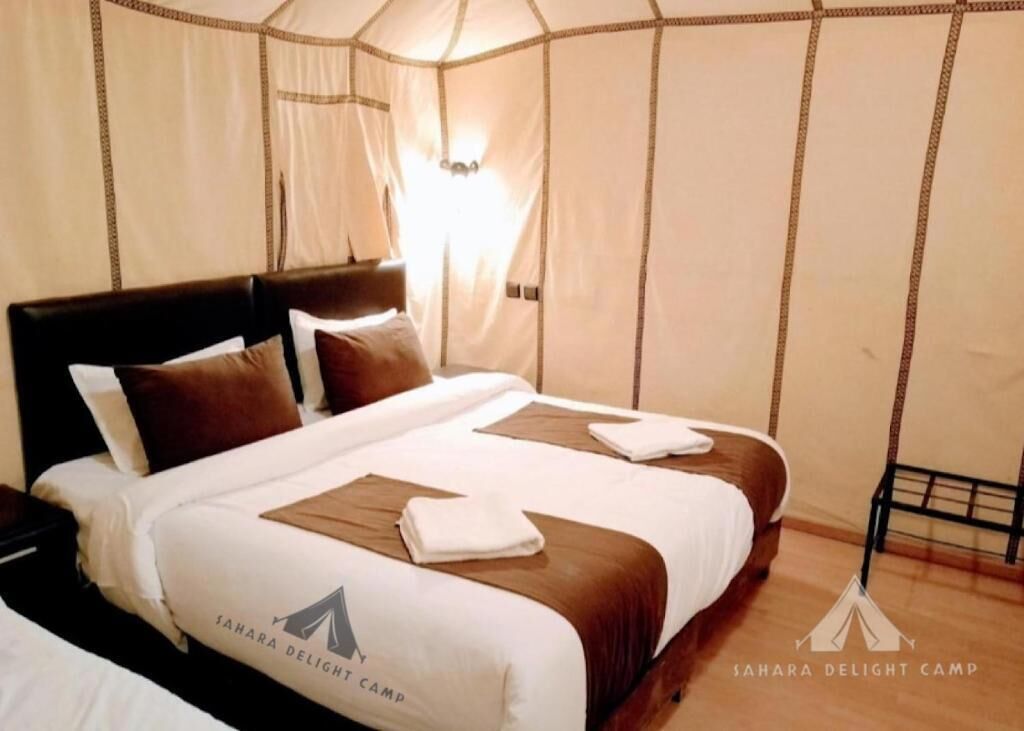 Een tweepersoonsbed met hoofdeinde, twee kussens en een dekbed. De kamer heeft een tentachtige constructie met een lichtbron in het midden.