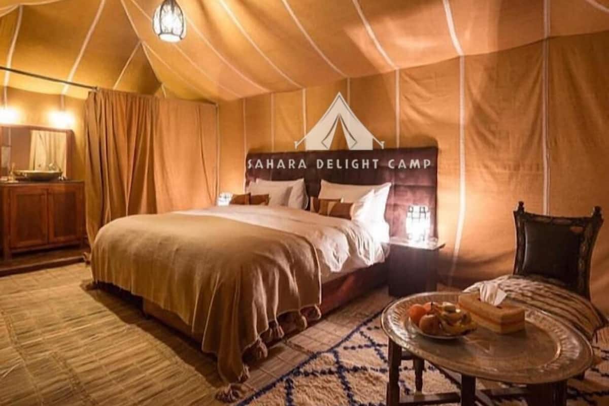 Een tent met een bed, een nachtkastje, een tafel met eten en een lamp.