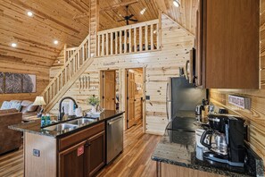 A wooden cabin interior with a kitchen, dining area, and a staircase leading to a loft. - Gatlinburg*Small but Spacious*WiFi*Hot Tub*Resort Amenities (Gatlinburg)