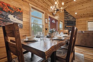 A wooden interior with a dining table set for four, a chandelier, and a fireplace. - Gatlinburg*Small but Spacious*WiFi*Hot Tub*Resort Amenities (Gatlinburg)