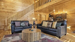 L’intérieur d’une cabane en rondins, avec un escalier, deux canapés en cuir, une table basse ronde et un plancher en bois.