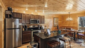 L’intérieur d’une cabane en bois comprend une cuisine équipée d’un réfrigérateur, d’un four à micro-ondes, d’une cuisinière et de tabourets de bar.