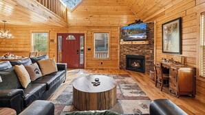 L’intérieur d’un chalet en bois comprend un canapé, une table basse, une cheminée, un téléviseur et un balcon.