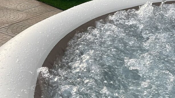 Ein Außenbereich mit Whirlpool, zwei Stühlen und einem Tisch, umgeben von einer Steinmauer und einem Zaun.
