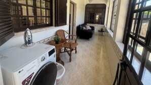 Ein Waschbereich mit einer LG-Waschmaschine, Korbstühlen, einem schwarzen Sofa und großen Fenstern mit dunklen Fensterläden.