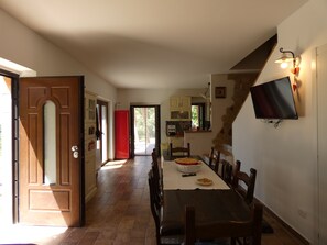 Ein Essbereich mit einem langen Tisch, Stühlen und einem an der Wand befestigten Fernseher.