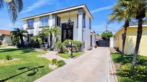 A two-story house with a front yard, palm trees, and a paved driveway. - Luxury Oasis Between Downtown LA & Orange County (Downey)