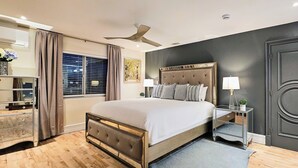 A bedroom with a large bed, a nightstand, a ceiling fan, a dark door, and a window with curtains. - Luxury Oasis Between Downtown LA & Orange County (Downey)