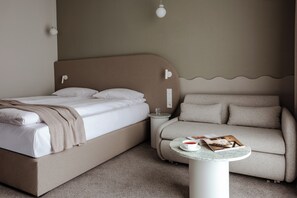 A bedroom with a bed, a sofa, a small table with a book and a cup, and a wall-mounted light fixture. - BELMONTE Hotel Ustronie Morskie (Ustronie Morskie)
