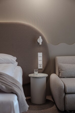 A modern bedroom with a curved headboard, a round bedside table with a glass, and a chair. - BELMONTE Hotel Ustronie Morskie (Ustronie Morskie)