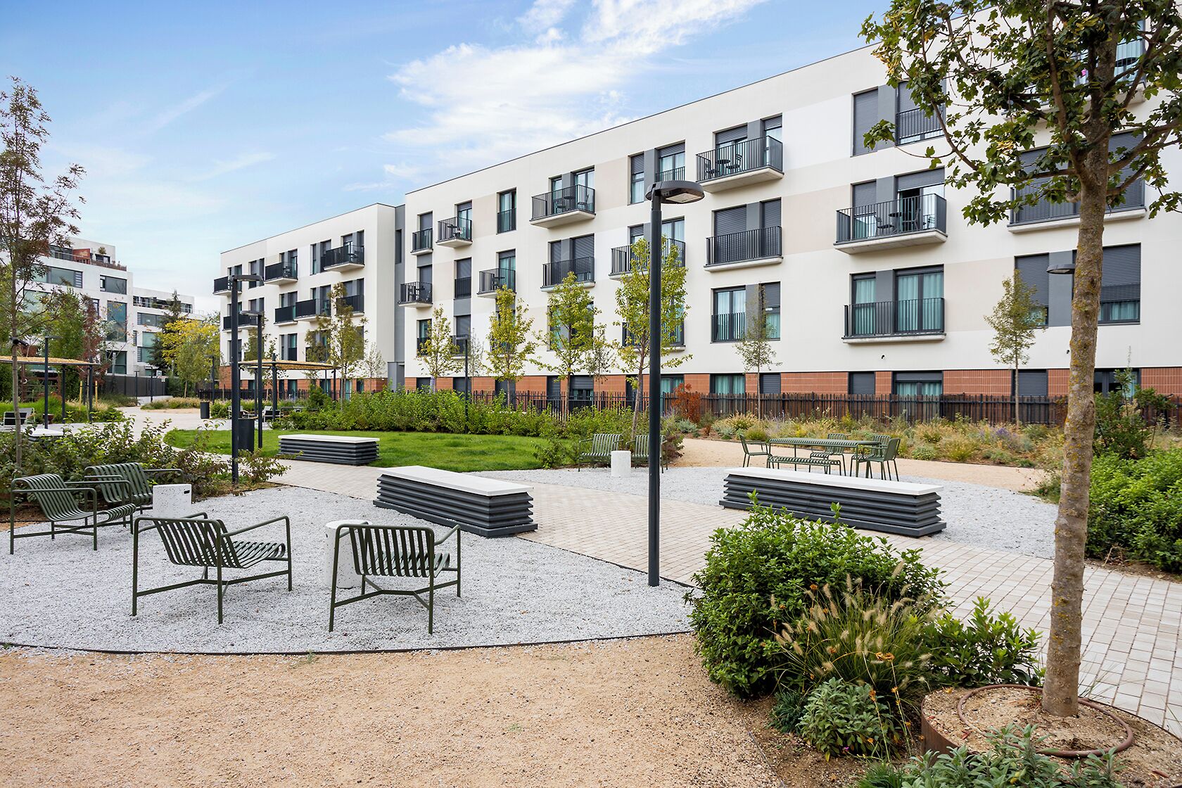 Un edificio de apartamentos moderno con asientos al aire libre, un jardín ajardinado y un patio de grava.