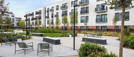 Un edificio de apartamentos moderno con asientos al aire libre, un jardín ajardinado y un patio de grava.