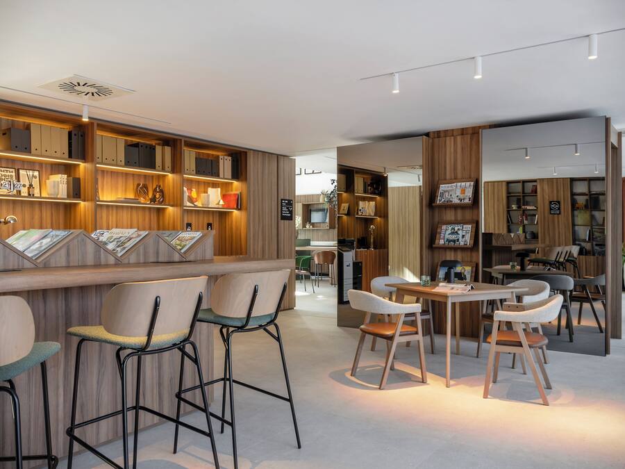 Un interior moderno con paneles de madera, taburetes de bar y una zona de comedor con sillas y una mesa.