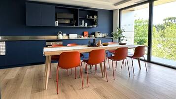 A modern kitchen with dark cabinetry, a wooden dining table, and red chairs.