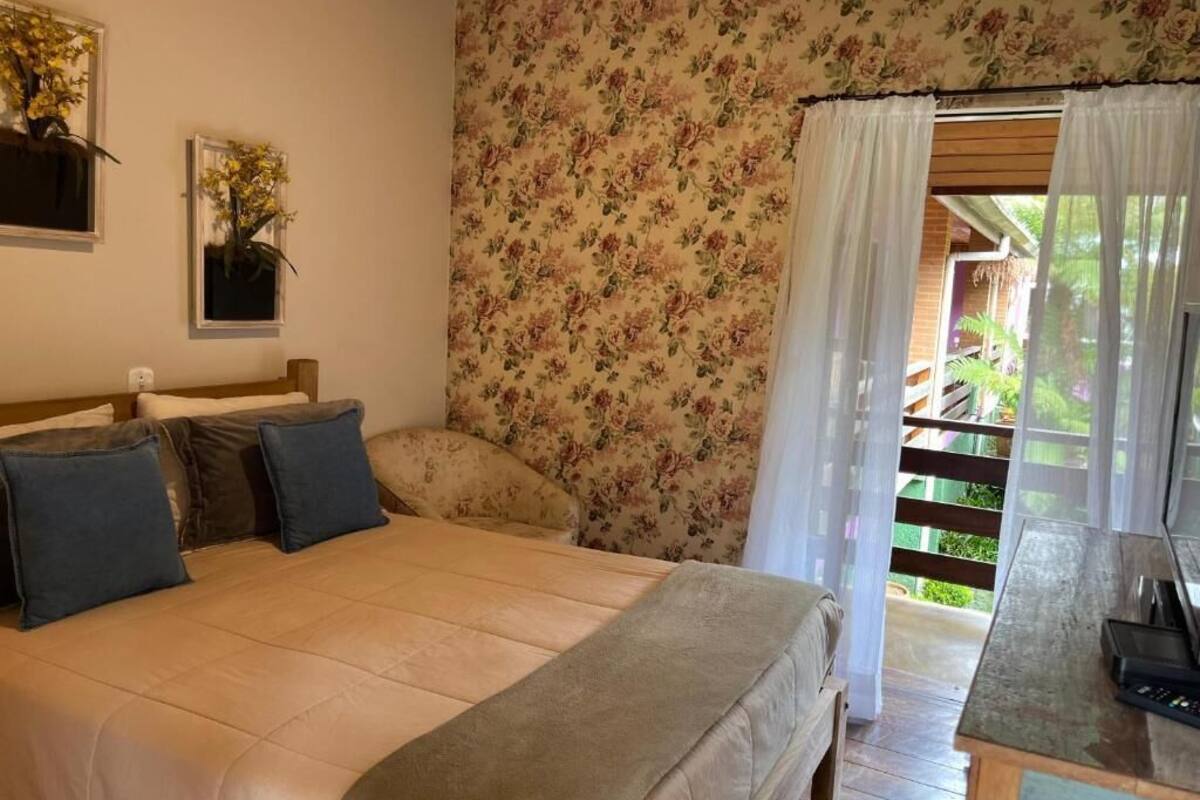 Un dormitorio con cama, cabecera de madera, mesita de noche y ventana con cortinas.
