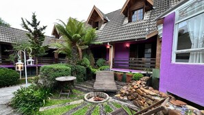 Un refugio rústico con un hogar de piedra, terraza de madera y abundante vegetación.