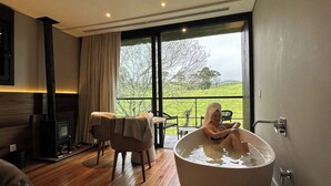 A modern room with a large bathtub, wooden flooring, a fireplace, and a view of a green landscape through large windows. - Fazenda Bom Retiro Hotel Boutique (Bom Retiro)