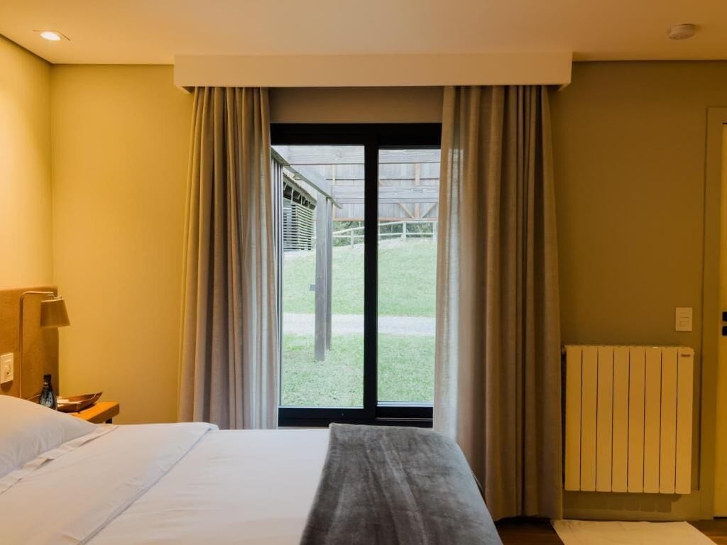 Habitación de hotel con cama, escritorio, silla, ventana con cortinas y vista a un edificio.