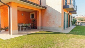 A covered outdoor dining area with a table and chairs, a small garden, and a building with a balcony. - Casa Sophie - One Bedroom Apartment, Sleeps 4 (Desenzano del Garda)