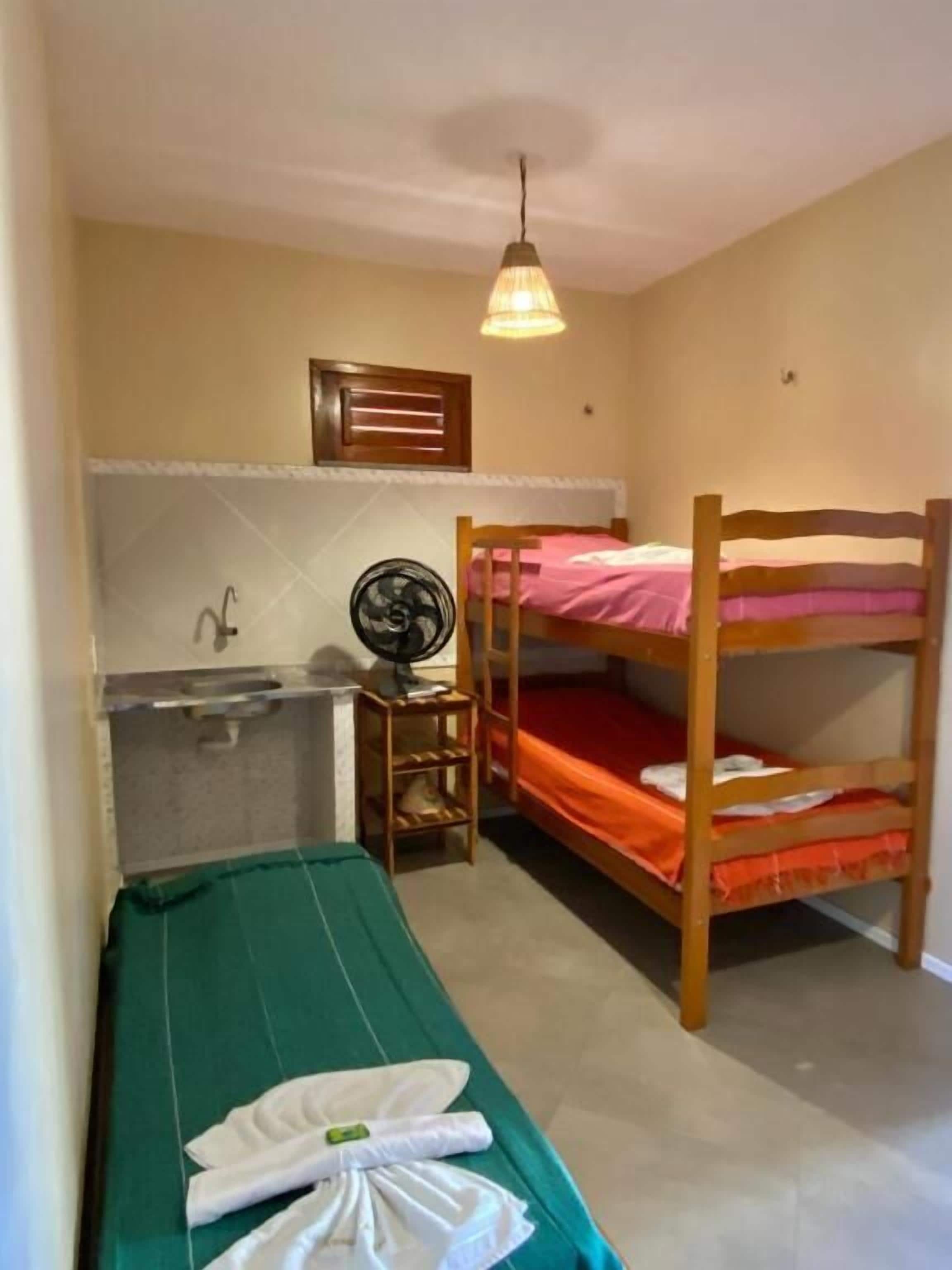 A small, compact room with bunk beds, a small table with a fan, a sink, and a ceiling light.