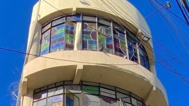 A building with a curved facade, a yellow sign with the text "POUSADA MUCURIPE" and a logo, and a large glass window with colorful patterns. - POUSADA MUCURIPE (Fortaleza)