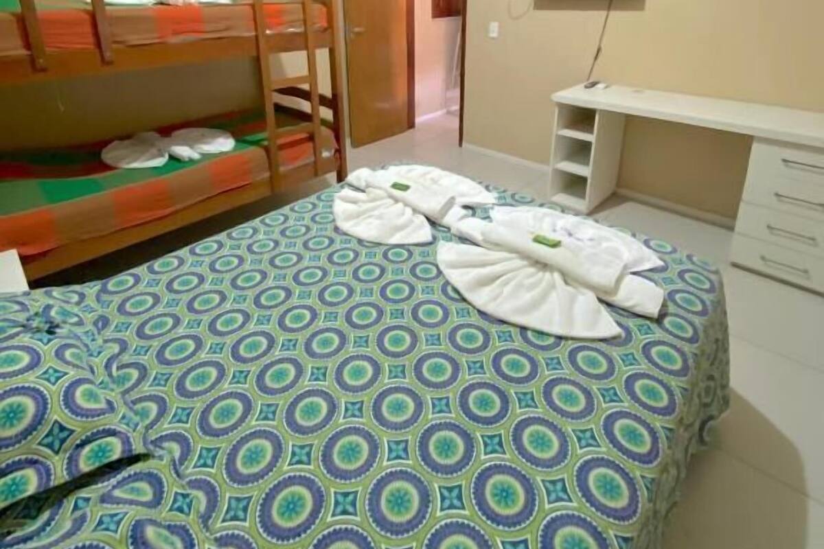 A room with a bunk bed, a desk, a flat-screen TV, and a patterned bedspread.