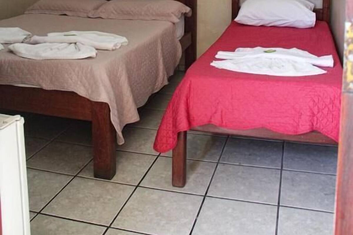 A room with two wooden beds, each with a different colored bedspread, and a painting on the wall.