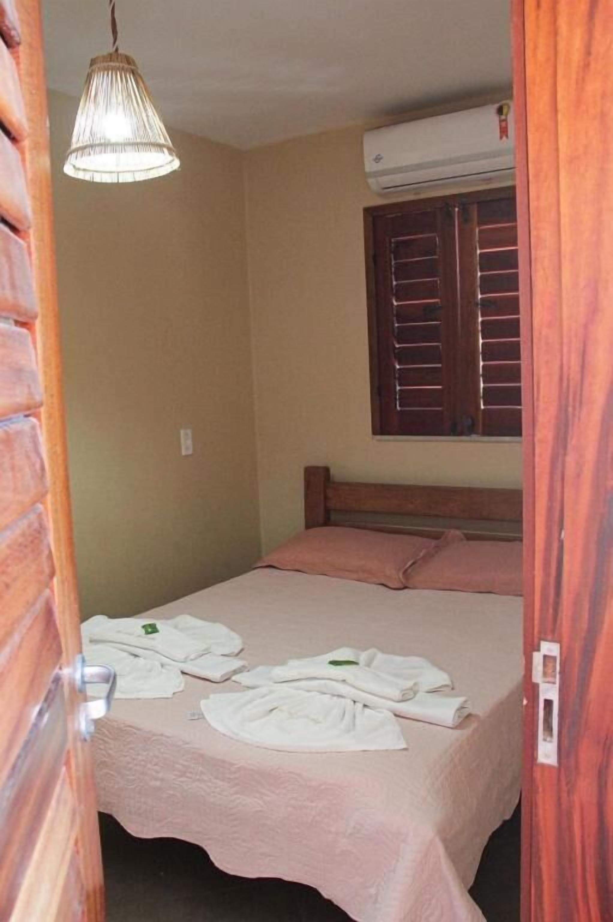 Un dormitorio con cama, lámpara colgante, aire acondicionado y ventana con persianas de madera.