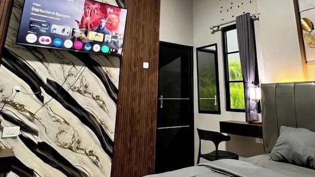 A modern bedroom with a bed, a TV mounted on the wall, a window with curtains, and a door. - KOSTEL H88 (Depok)