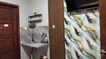 A bedroom with a bed, a wooden wardrobe, a bathroom with a sink and mirror, and a TV mounted on the wall.