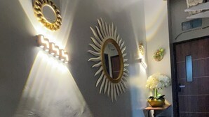 A hallway with a wooden floor, a mirror with a sunburst design, and wall-mounted lights. - KOSTEL H88 (Depok)