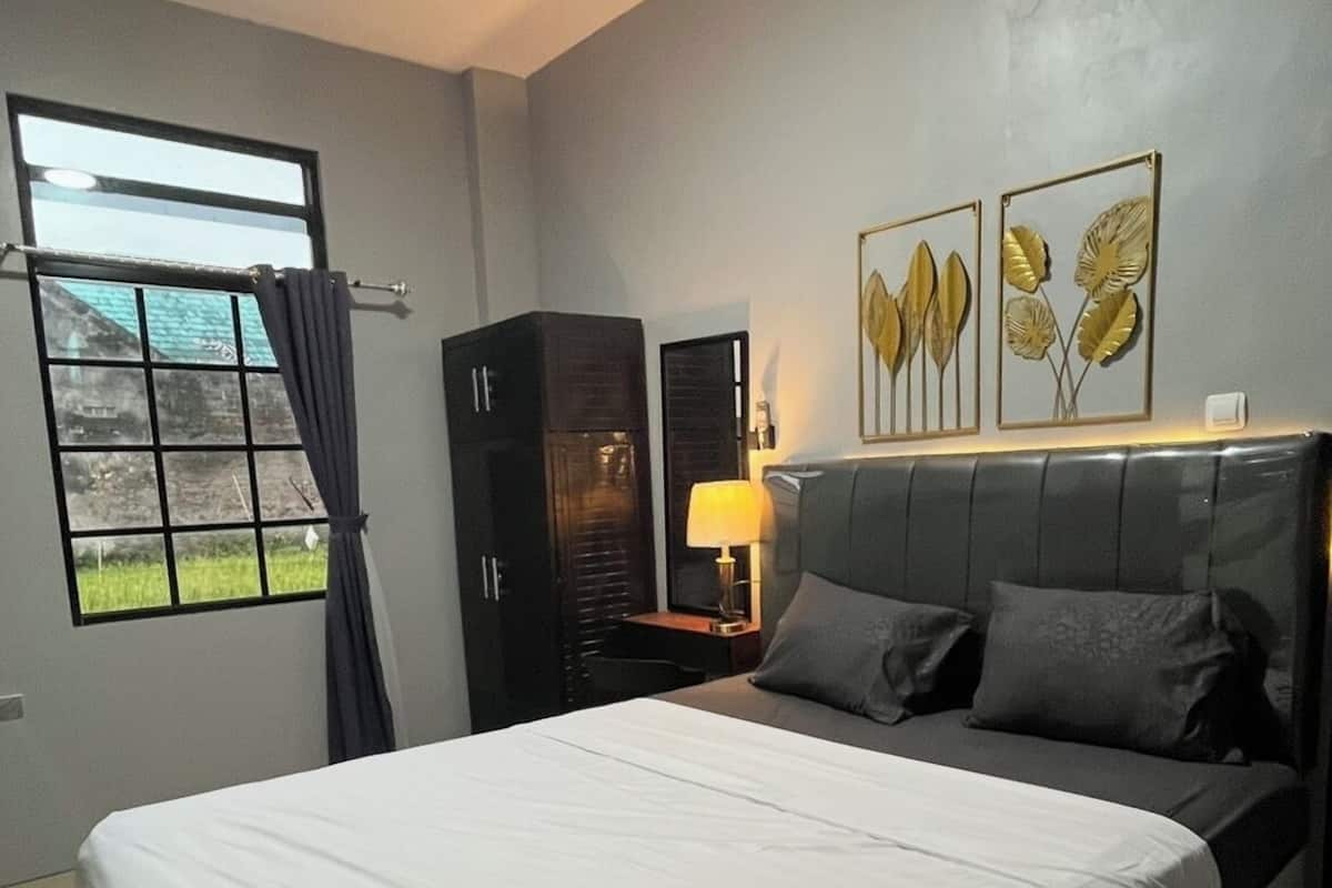 A bedroom with a large bed, a nightstand, a lamp, a wardrobe, and a window with curtains.