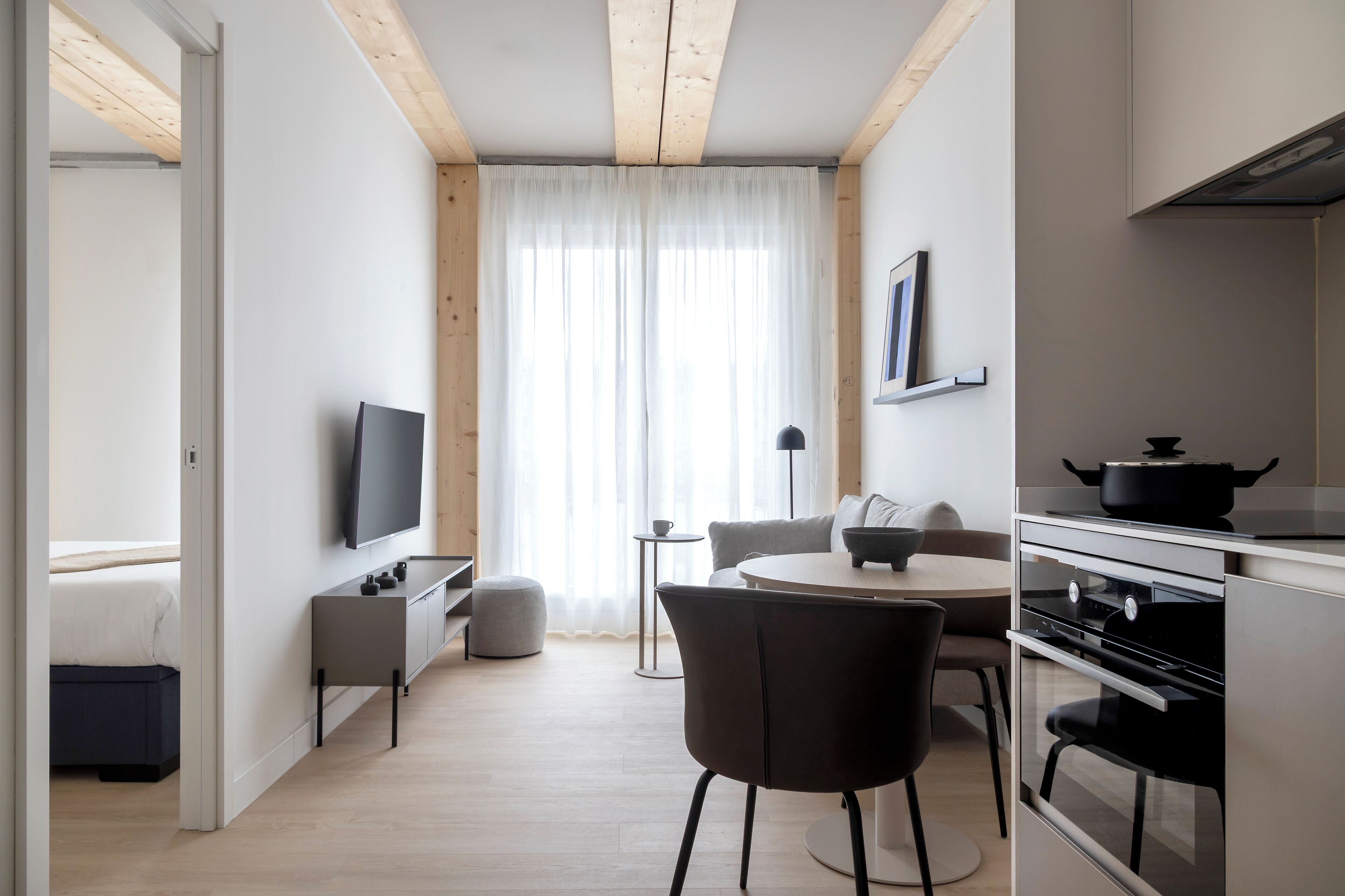 Una cocina moderna con comedor, televisor y un amplio ventanal con cortinas ligeras.