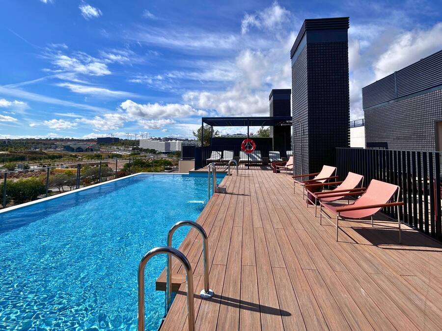 Uma área de piscina no terraço com deck de madeira, espreguiçadeiras e vista para a cidade.