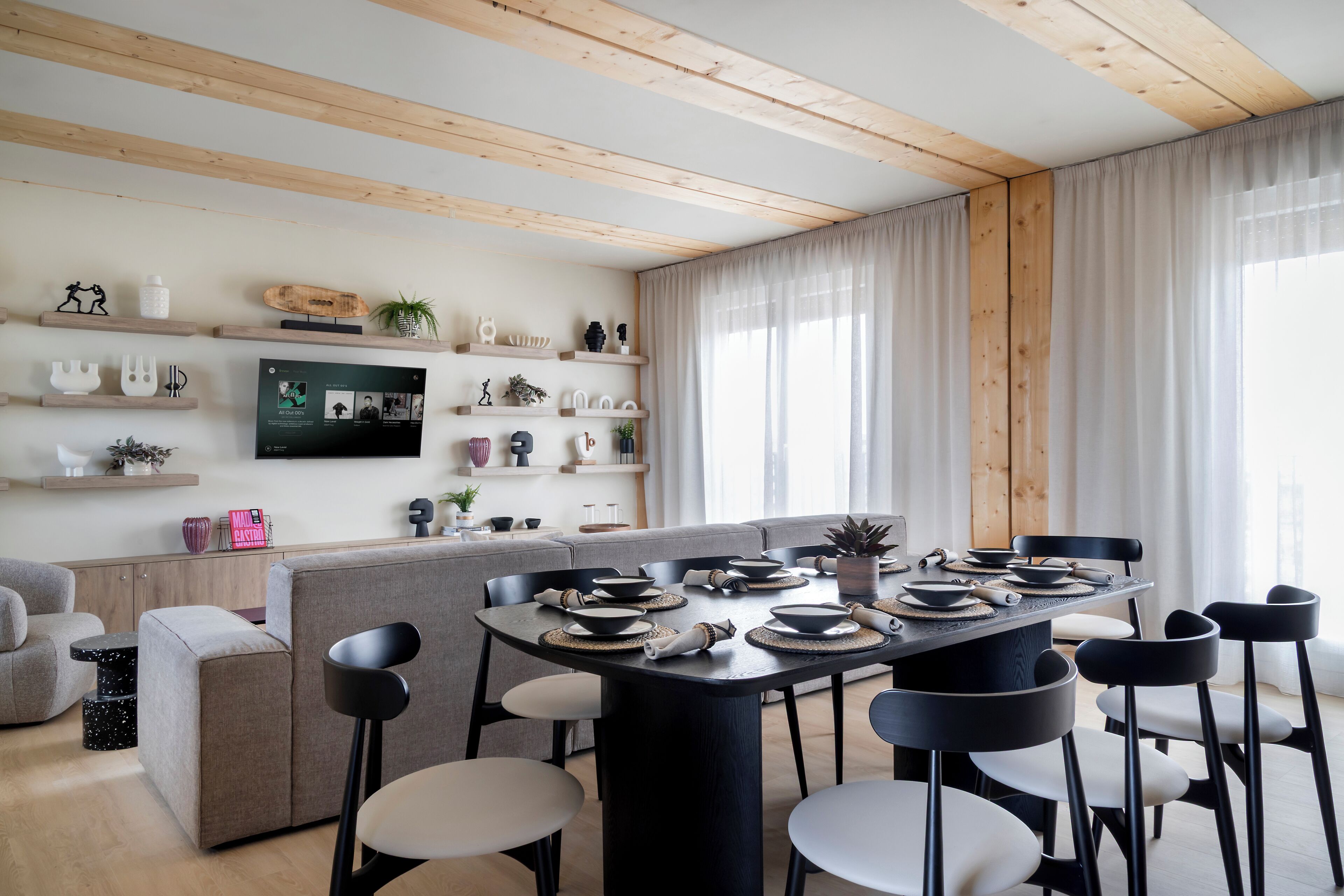Un espace repas moderne avec une table ronde dressée pour six personnes, entourée de canapés gris et de chaises noires.