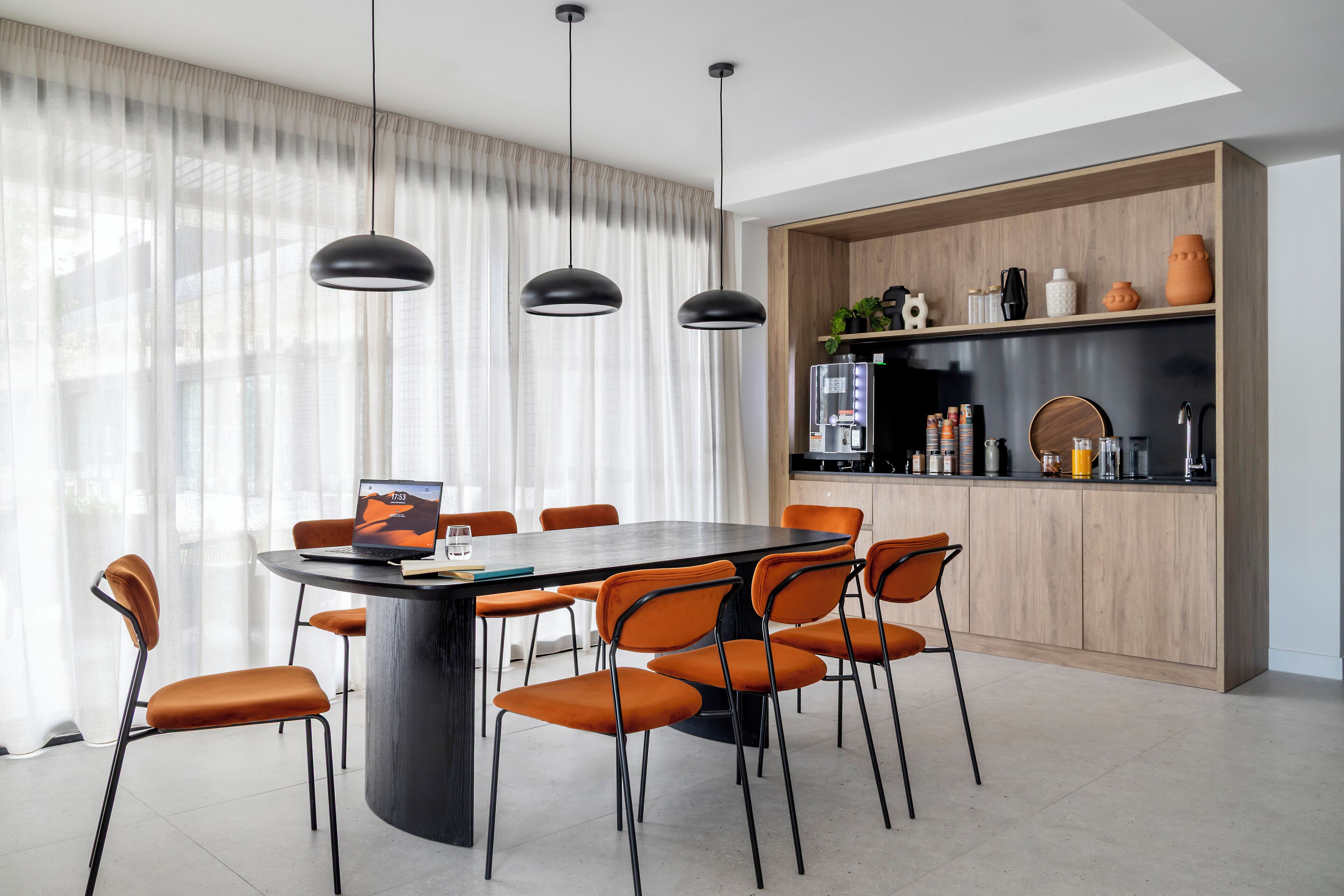 A modern dining area with a round table, orange chairs, and pendant lighting.