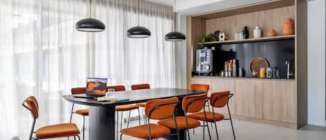 A modern dining area with a round table, orange chairs, and pendant lighting.